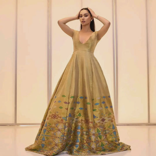 Woman wearing a long, elegant yellow dress with intricate patterns against a neutral background