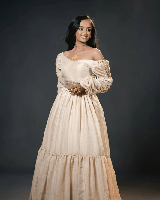 Woman wearing a beige off-shoulder dress against a dark background