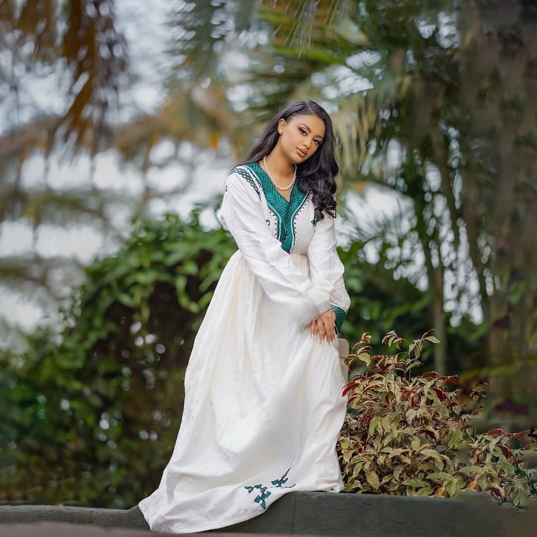 Woman in a white dress with green accents standing outdoors among plants