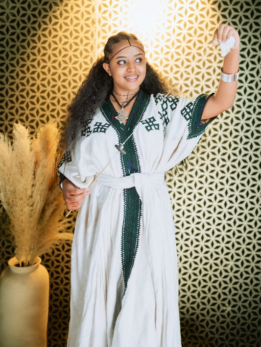 Woman in a white and green dress standing against a decorative wall.