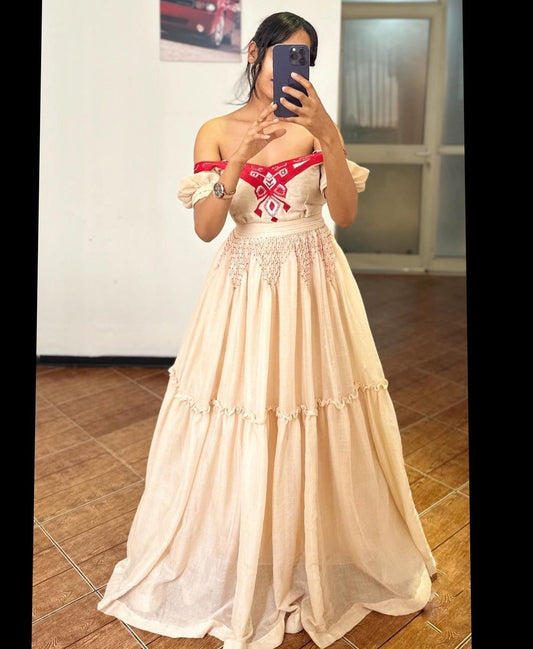 Woman wearing a beige off-shoulder dress with a red belt in a room.