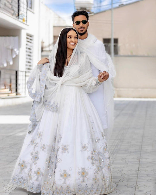 Two people in white traditional outfits standing outdoors.