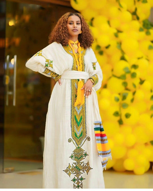 Woman wearing a white dress with colorful embroidery in front of yellow flowers.