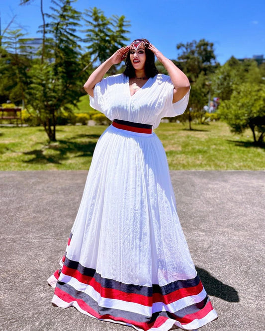 Woman in a white dress with red and blue accents standing outdoors on a sunny day.