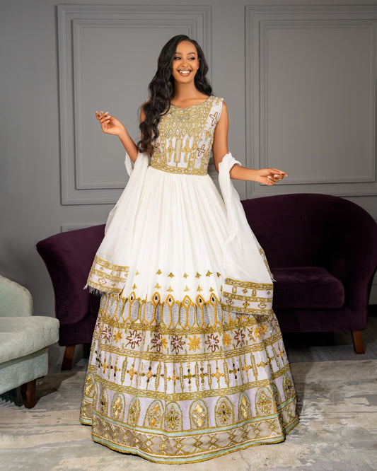Woman wearing a white and gold traditional outfit in a room with purple chairs.