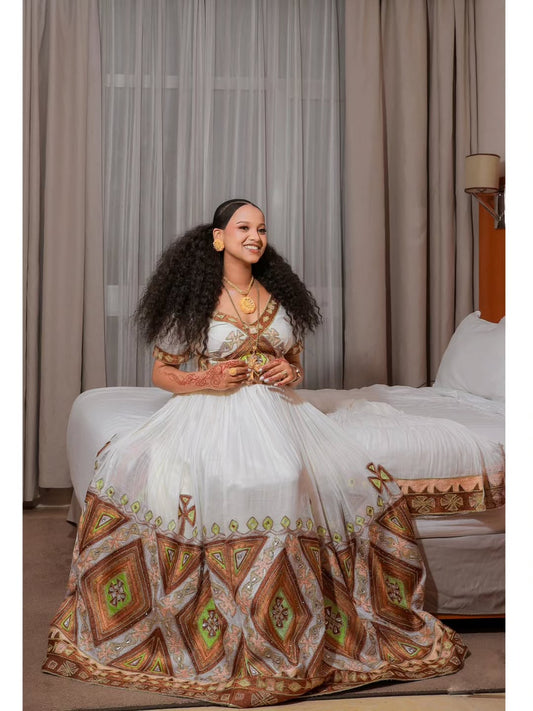 Woman in a white and patterned dress sitting on a couch with curtains in the background
