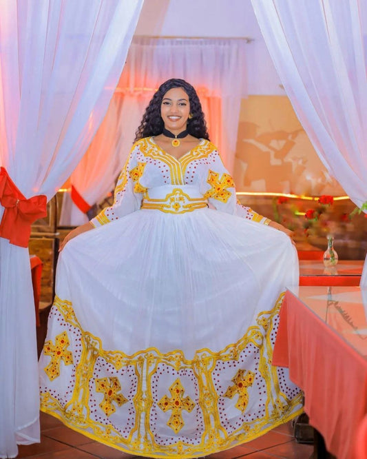 Woman in a white and yellow traditional outfit sitting in a decorated room.
