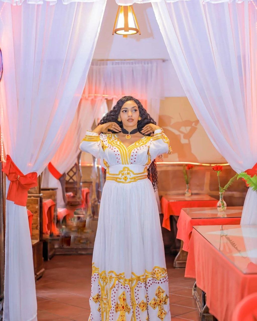 Woman in a white and gold dress standing in a decorated room with red and white decor.