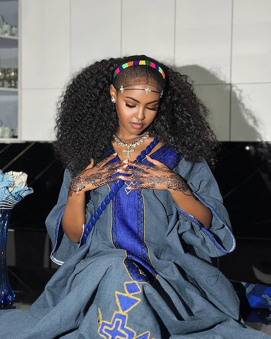 Woman in a blue traditional outfit with intricate henna designs on her hands, sitting indoors.