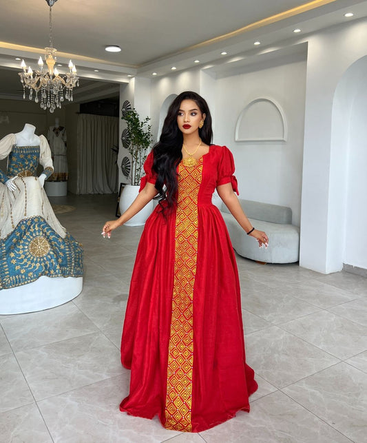 Woman in a red dress with gold patterns standing in a stylish interior setting.