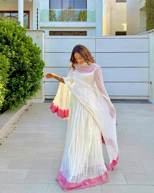 Woman in a white and pink saree standing outside a building.