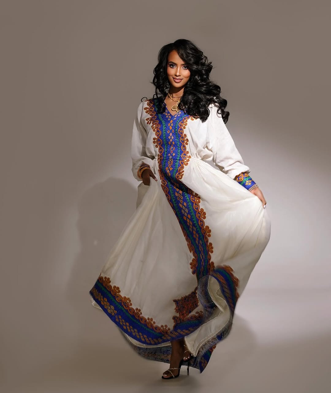 Woman wearing a long, embroidered dress with a white background