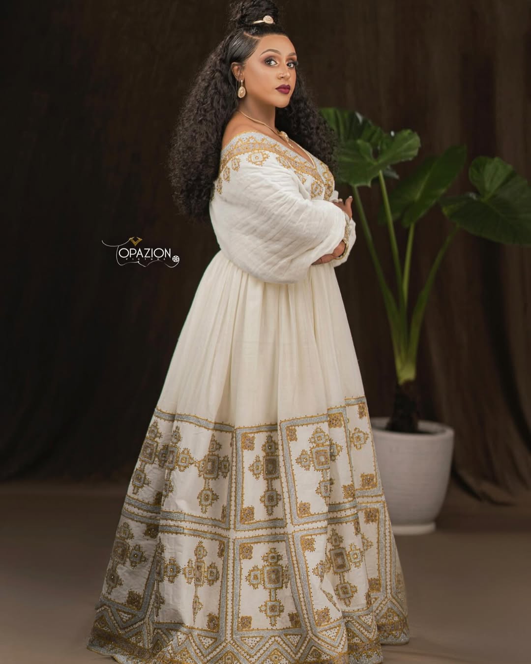 Woman in a white and gold traditional outfit with a plant in the background