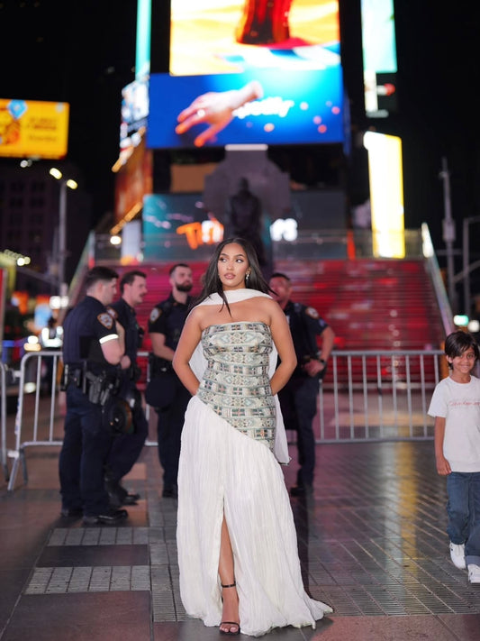 Woman in a strapless dress with a high slit walking in Times Square at night.