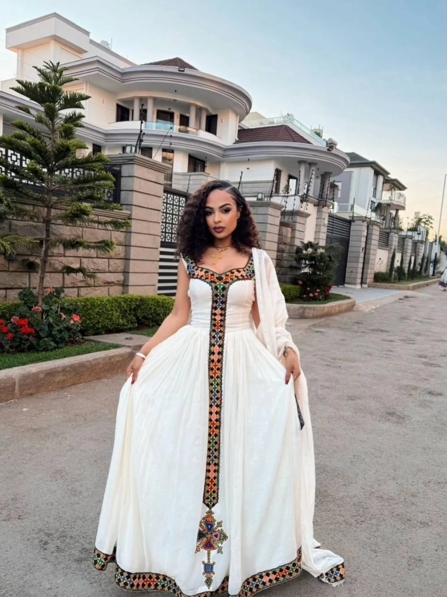 Woman in a white dress with decorative patterns standing on a street.