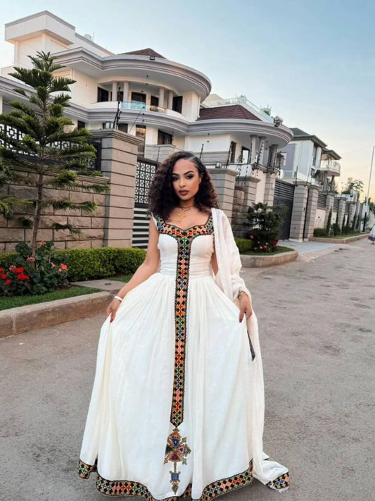 Woman in a white dress with decorative patterns standing on a street.
