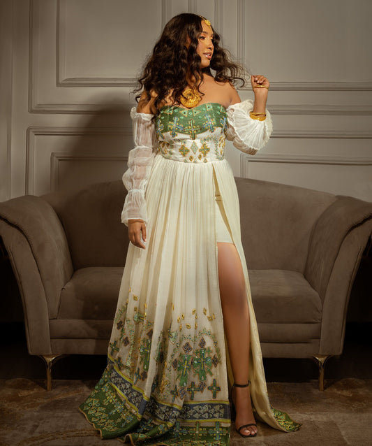 Woman in a long, elegant dress with floral patterns in a room with a gray sofa.