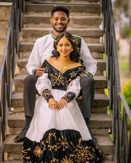Couple sitting on stone steps wearing traditional attire with intricate designs.