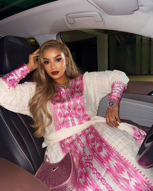 Woman in a pink and white patterned dress sitting inside a car.