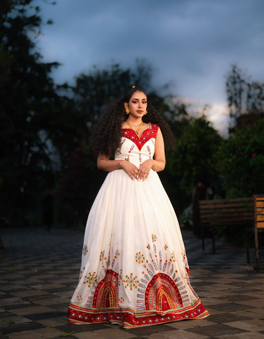 Woman in a white and red dress with intricate patterns standing outdoors.