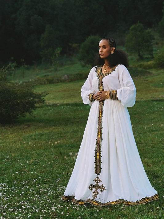 Woman in a white dress with gold accents standing in a grassy field.