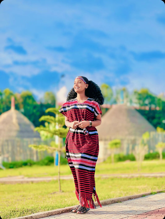 Woman in a striped dress standing outdoors with greenery and blue sky in the background