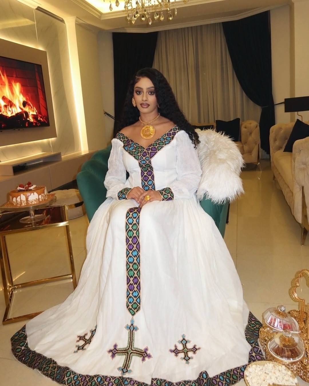 Woman in a white dress with intricate patterns in a luxurious room.