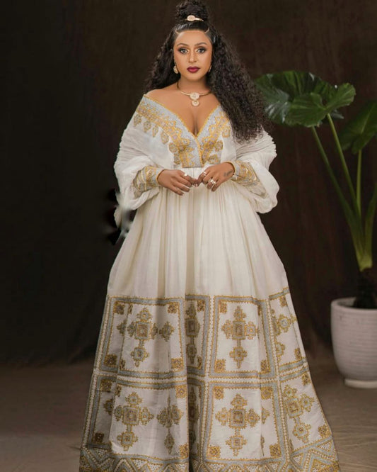 Woman wearing a white dress with gold embroidery in a dark setting