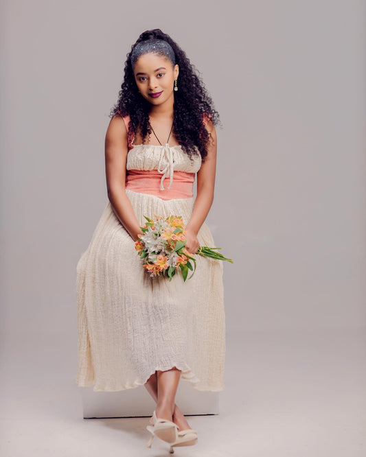 Woman in a white and pink dress holding flowers against a plain background