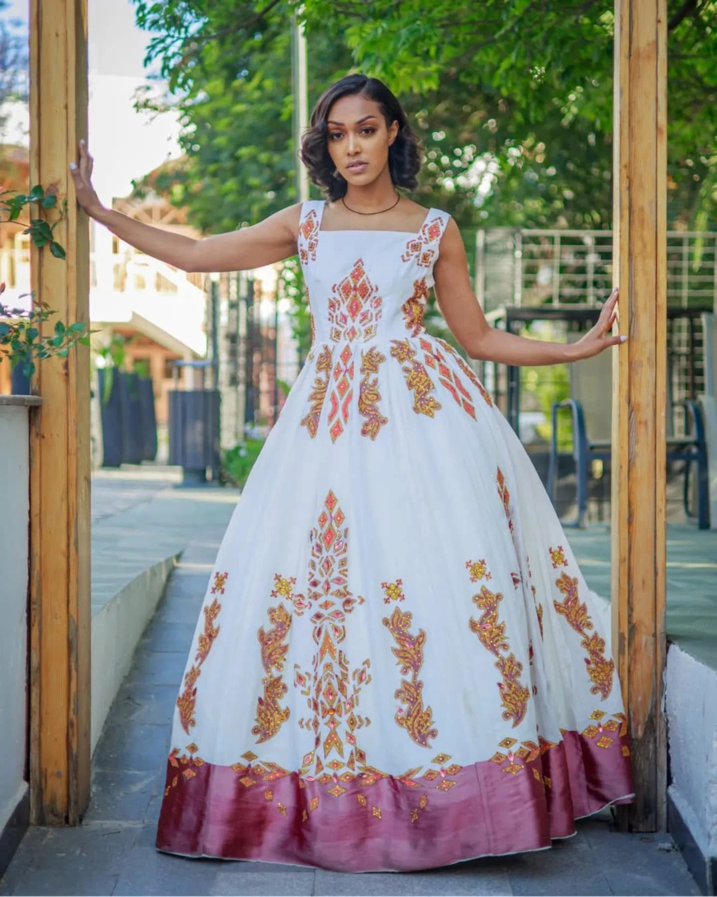 Woman in a white dress with orange floral patterns standing in front of a wooden door.
