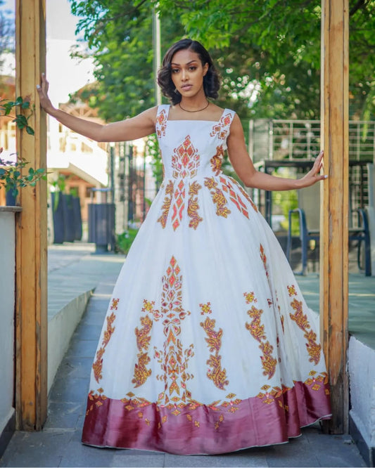Woman in a white dress with orange floral patterns standing in front of a wooden door.