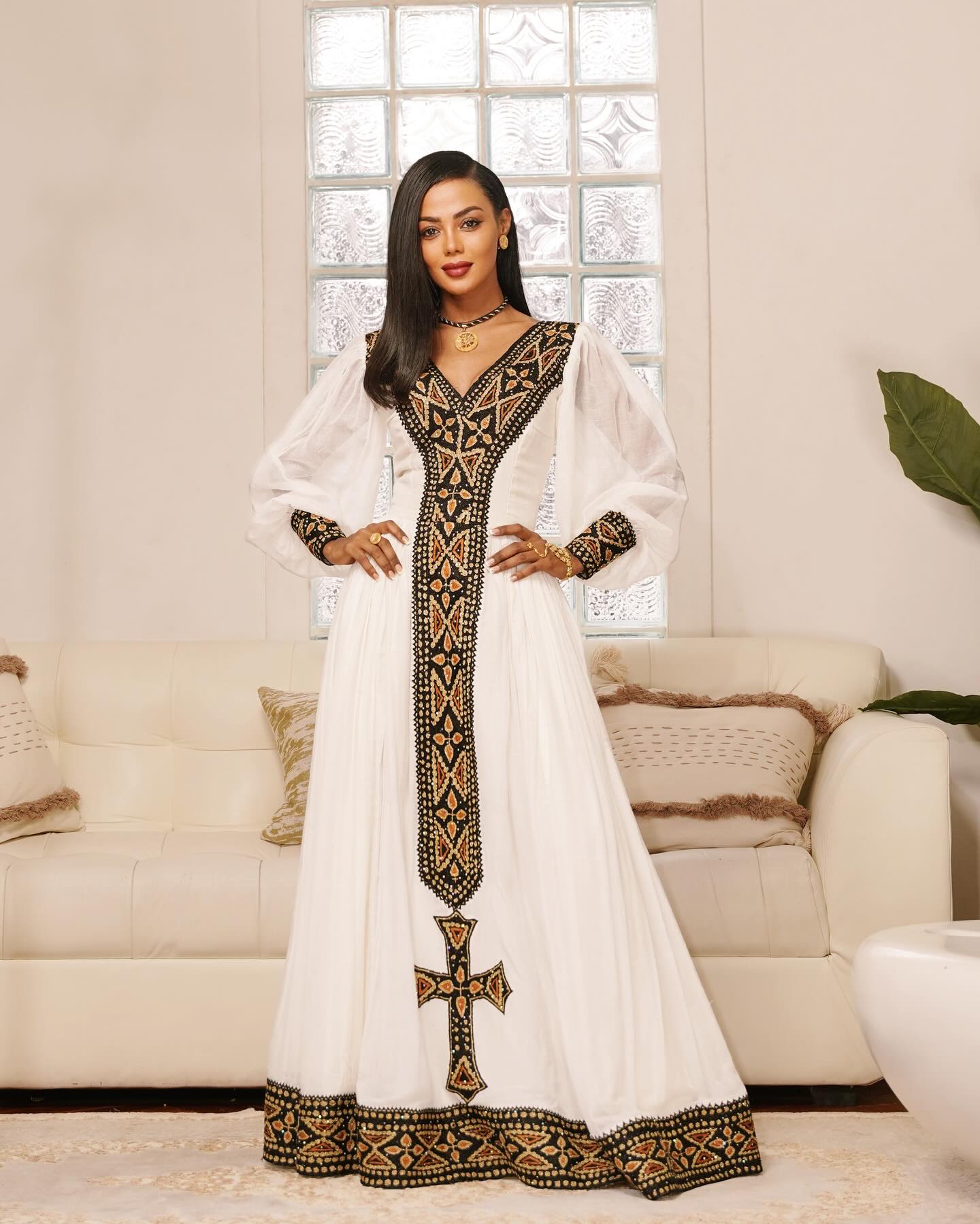 Woman wearing a white dress with black embroidery in a living room setting
