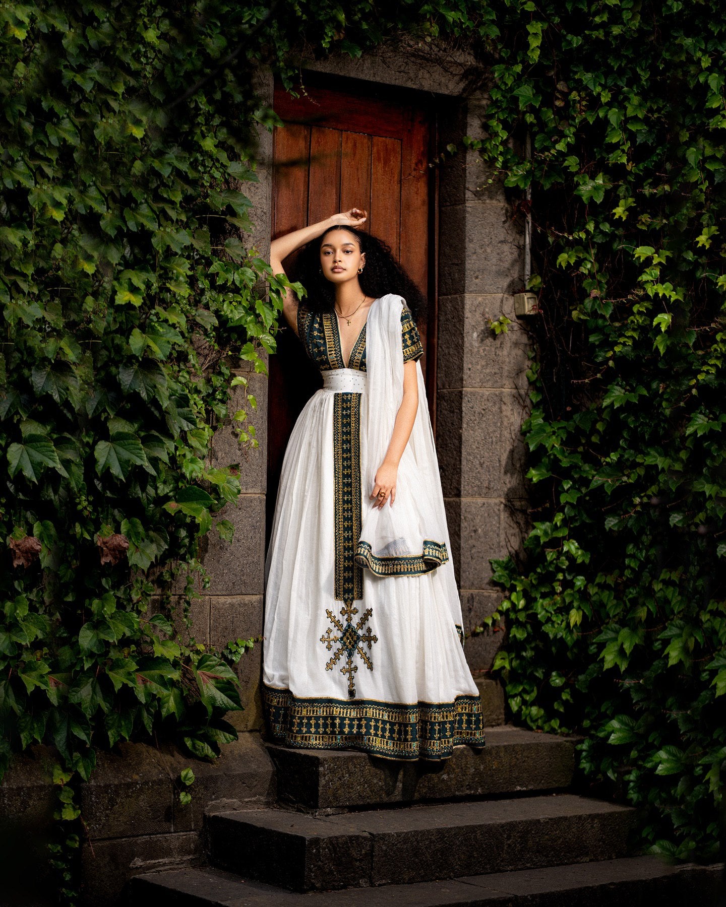 Woman in a traditional outfit standing in a doorway surrounded by greenery