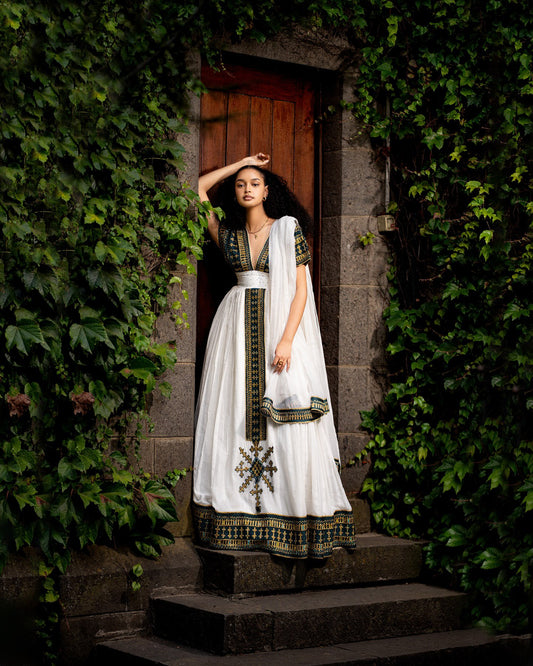 Woman in a traditional outfit standing in a doorway surrounded by greenery